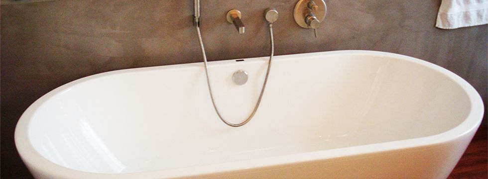 Freistehende Badewanne vor einer fugenlos verputzten Wand mit Wandarmatur