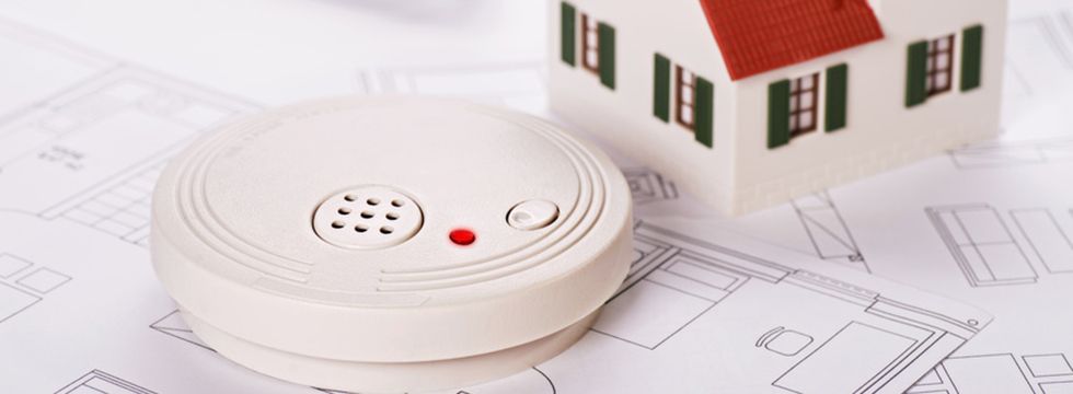 Rauchmelder auf einem Grundrissplan neben einem Hausmodell