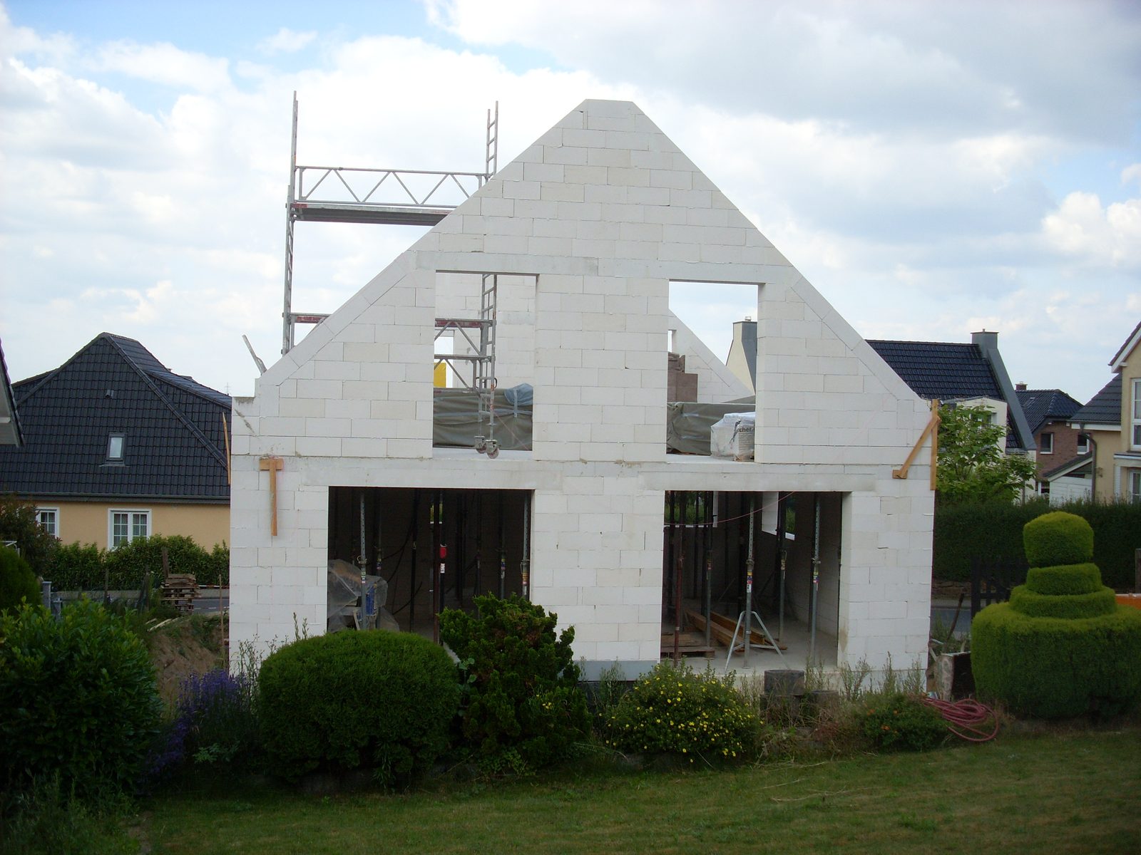 Rohbau eines Einfamilienhauses aus weißem Kalksandstein mit Giebelwand, Fensteröffnungen, Deckenstützen und Gerüst